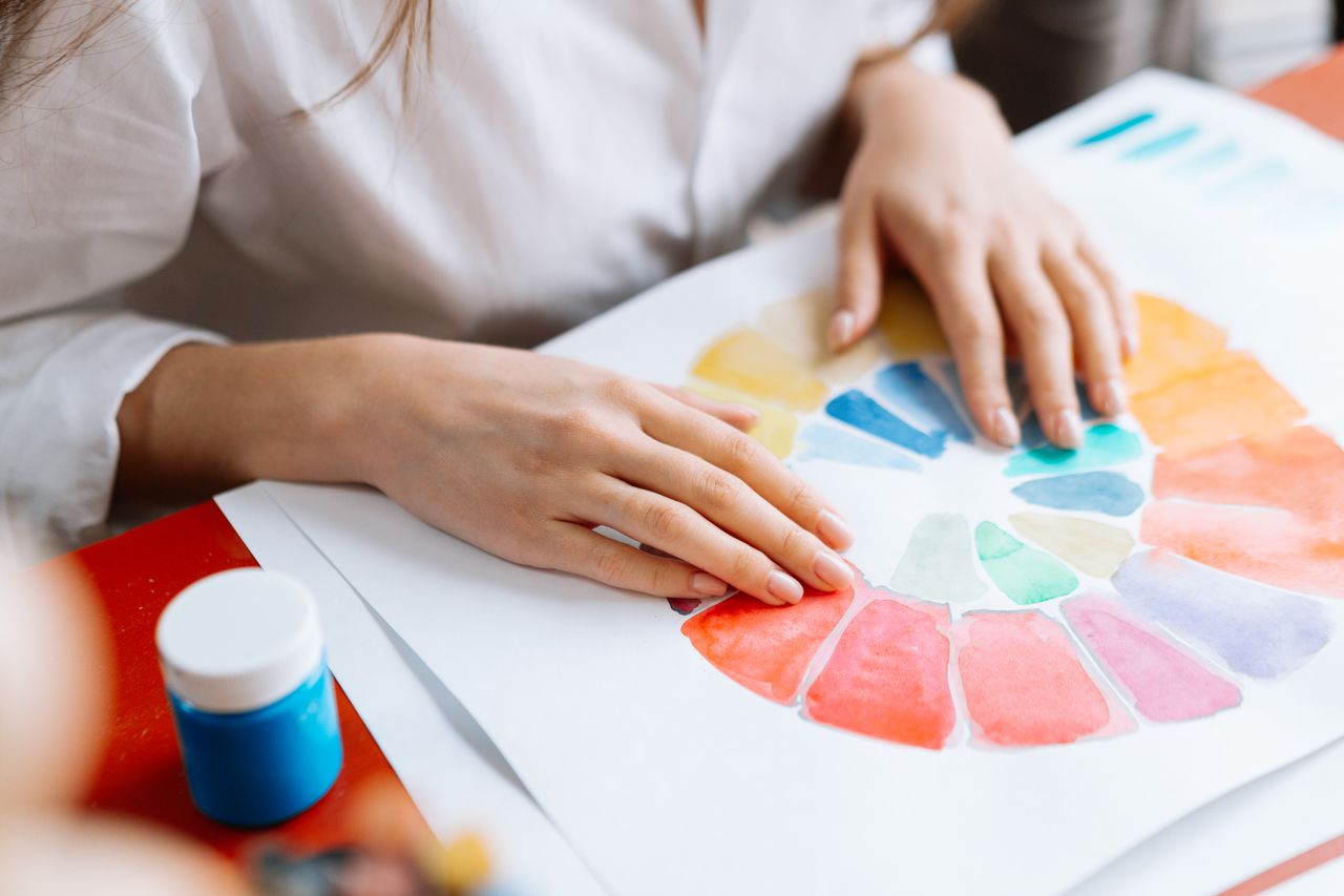 Artistic hands arranging a vibrant color wheel on paper, showing creativity and color theory.