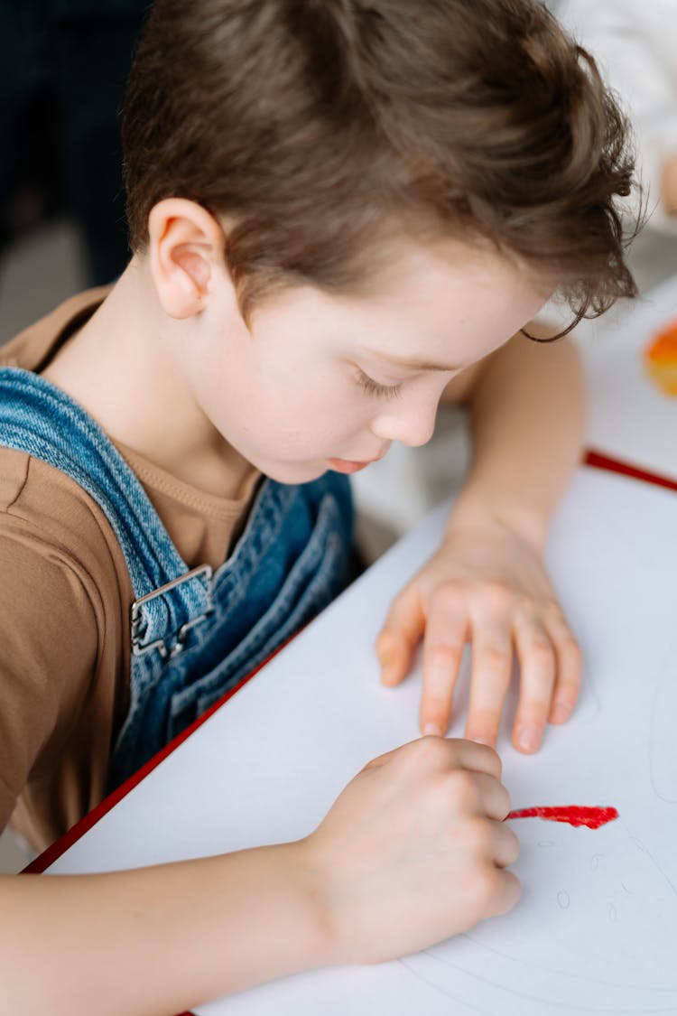 A Boy In Brown Shirt Drawing On White Paper