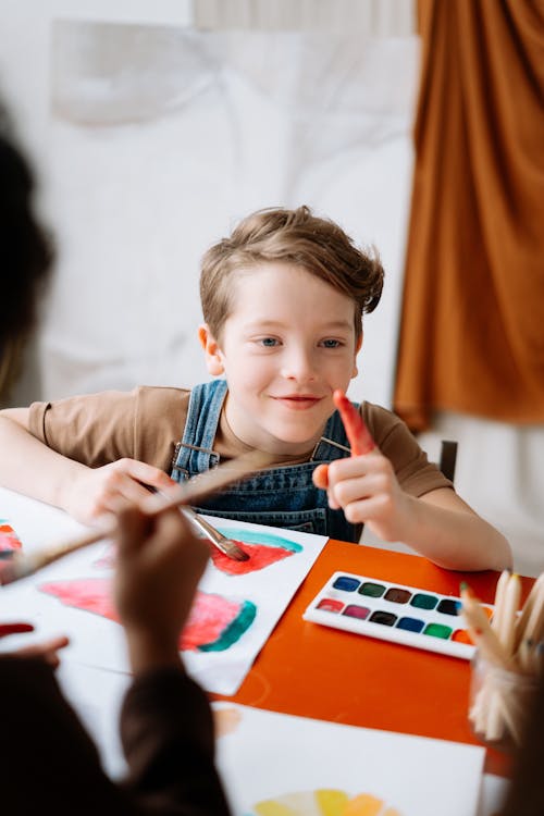 A Young Boy on Brown Shirt Smiling while Sitting Near the Table