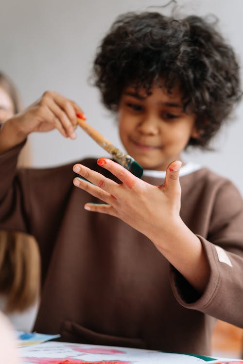 Little Boy Painting His Hand with a Paintbrush 