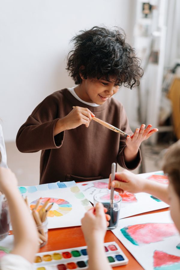 Young boy smiling while painting his hands with bright colors