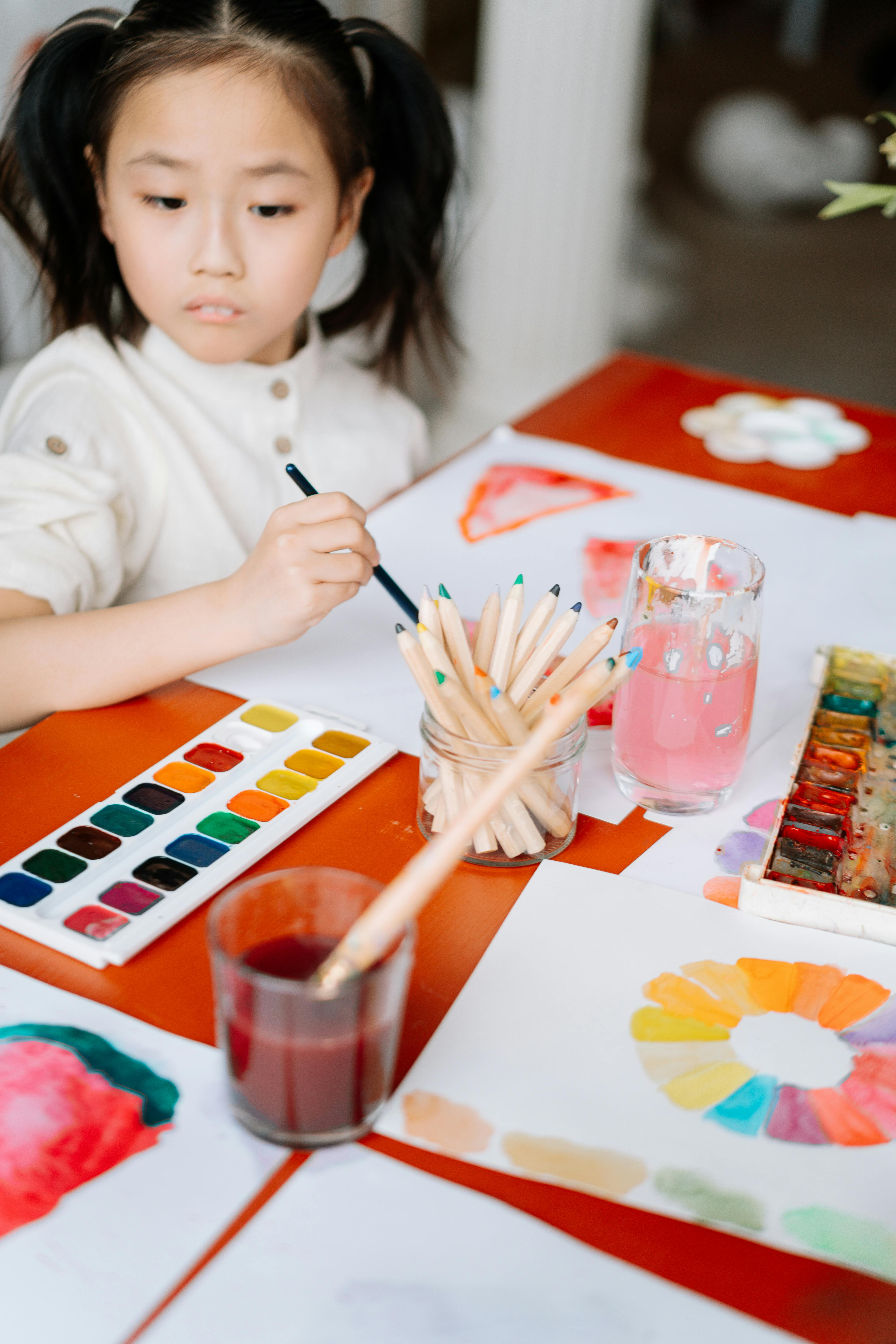 a young girl looking at the watercolor on the table