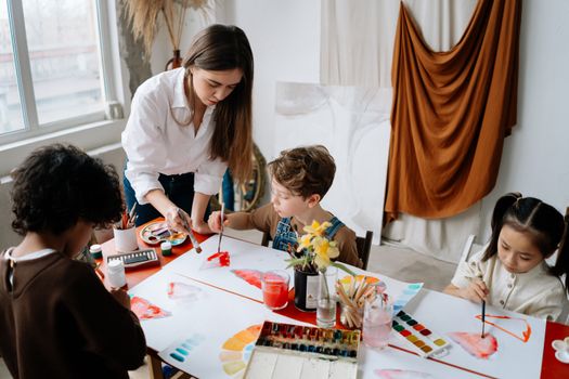 A group of children engaging in an art workshop with a teacher, using paintbrushes and colors.