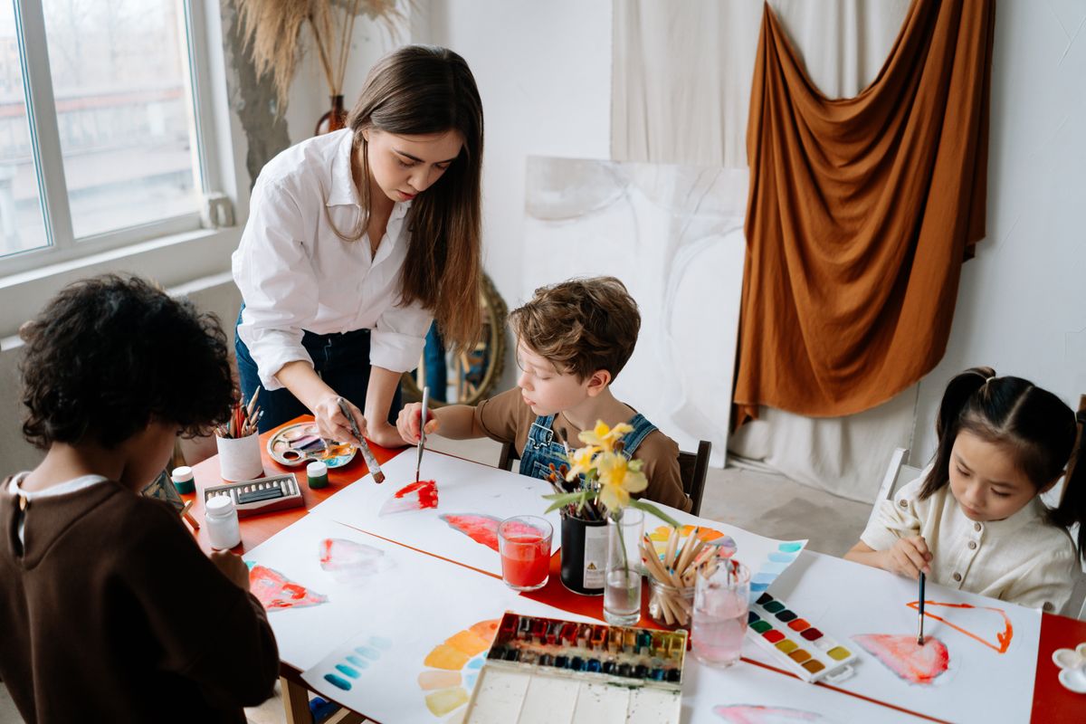 Children painting together at an art table with their teacher