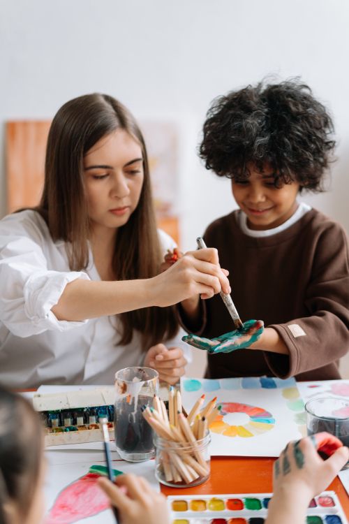 Free A teacher and child painting with brushes and watercolors in a creative classroom setting. Stock Photo