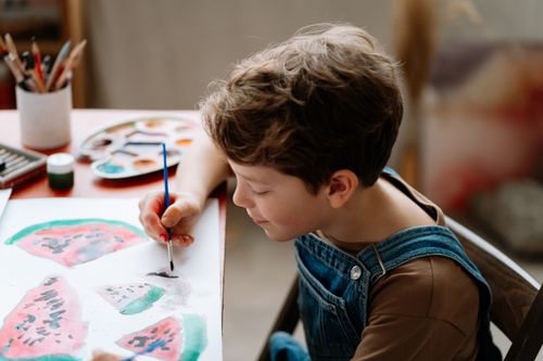 Free Young boy painting watermelon slices with watercolors during art lesson. Stock Photo