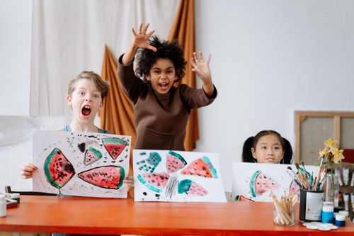 Free Joyful children displaying watermelon artwork in an interactive art class indoors. Stock Photo