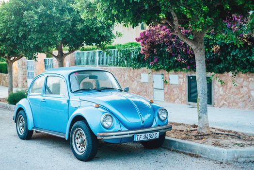 Classic blue Volkswagen Beetle parked under trees in a sunny Spanish street setting.