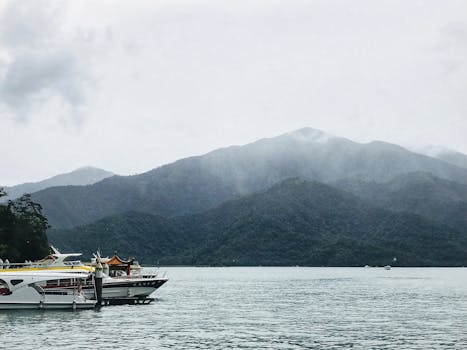 A tranquil scene of boats docked at Sun Moon Lake, surrounded by misty mountains in Taiwan. by 영 봄