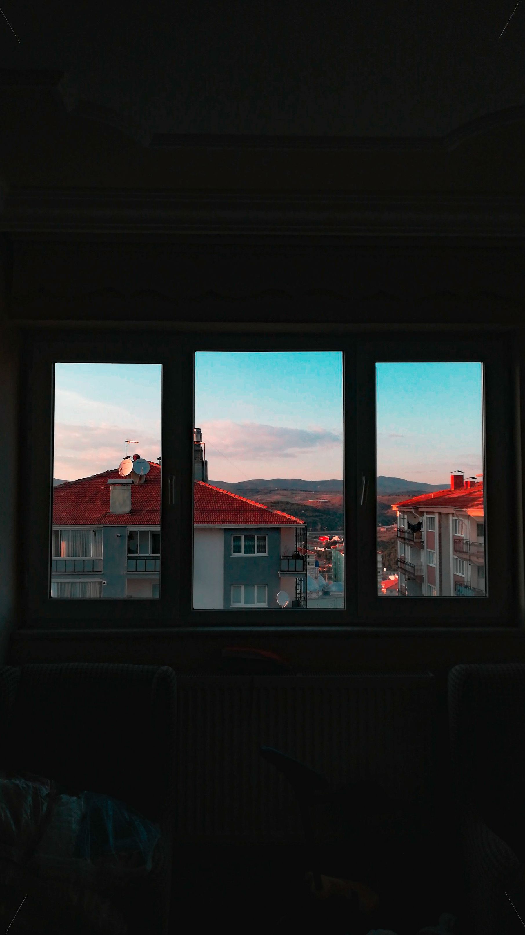 A beautiful sunset view of Uşak city's rooftops and distant hills through a window.