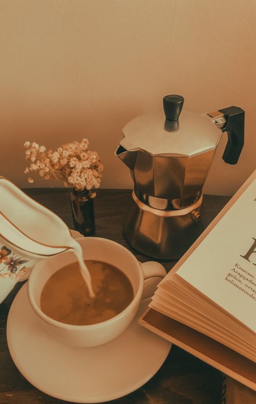 Free Rustic coffee scene with a moka pot, pouring milk, flowers, and an open book. Stock Photo