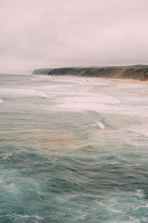 Free A breathtaking view of ocean waves crashing against coastal cliffs under a cloudy sky. Stock Photo