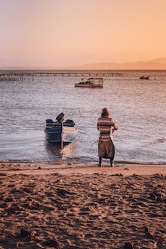 Fisherman pulling a boat ashore at sunset on a peaceful beach.