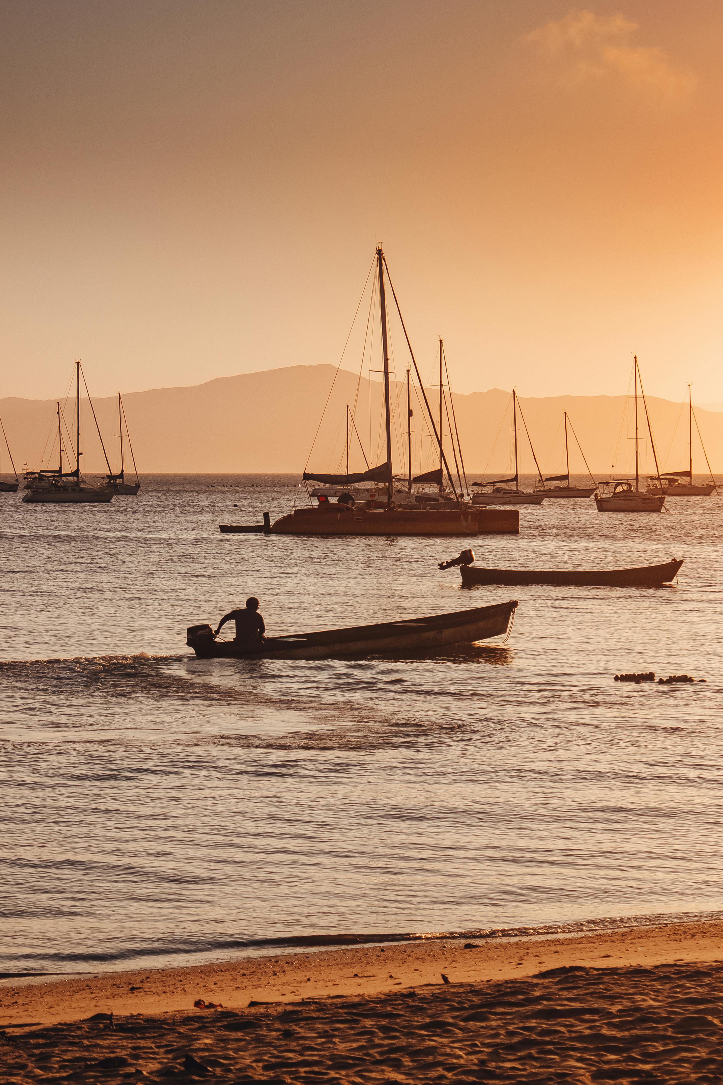 Scenic view of boats silhouetted against a warm sunset on a calm sea, perfect for travel inspiration.