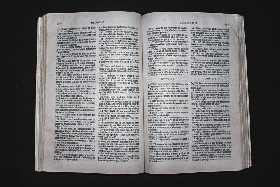 An open Bible displaying chapters of Acts in Spanish and English, photographed from above.
