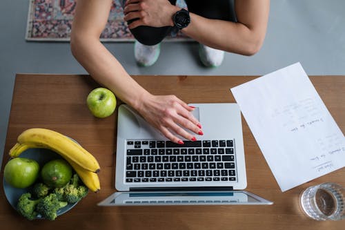 A Person in Front of the Laptop Near a Plate of Fruits and Vegetables