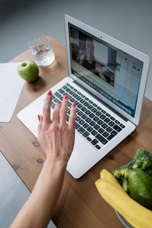 Free A woman in a video call on a laptop with fruits and vegetables on a wooden table. Stock Photo Free A woman in a video call on a laptop with fruits and vegetables on a wooden table. Stock Photo