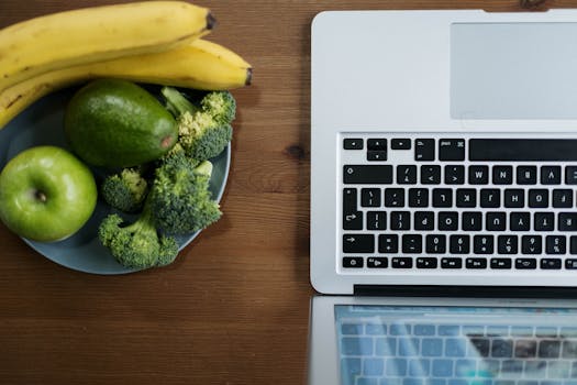 Flatlay of fresh fruits and vegetables with a laptop on a wooden table.