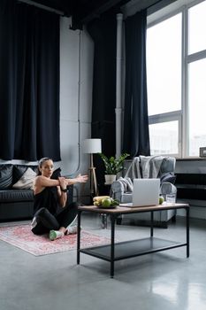 Woman practicing yoga indoors with a laptop in cozy living space, embracing modern wellness.