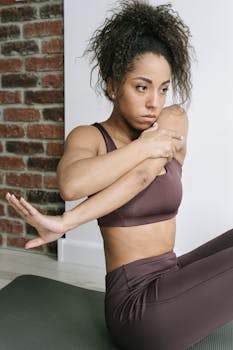 Young woman in brown activewear performing yoga stretch on mat indoors.