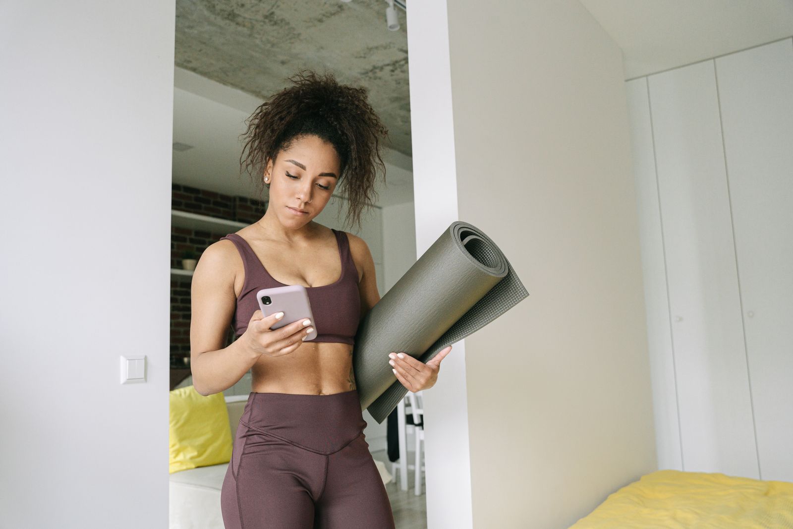 Young woman holding a yoga mat while checking a free yoga app on her smartphone before a home practice