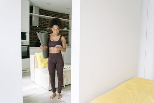 Woman in Fitness Wear Standing Holding Cell Phone and Mat