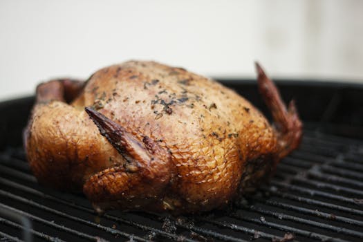 Close-up of a perfectly grilled whole chicken on a BBQ grill, showcasing crispy skin and herbs.