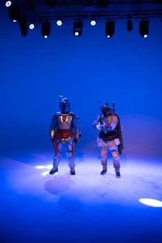 Two cosplayers dressed as futuristic bounty hunters in a dramatic blue-lit studio setting.