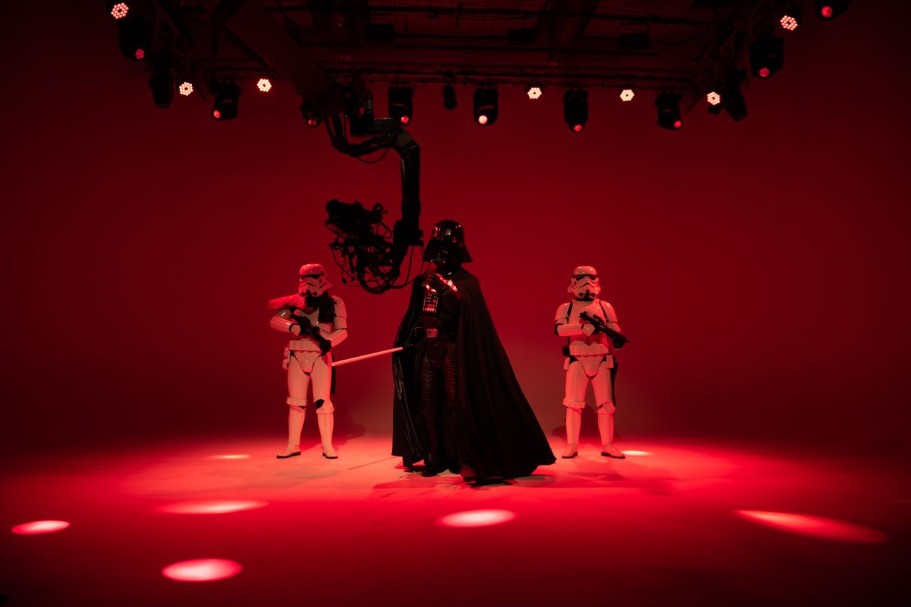 three sci fi characters in costumes pose under red studio lights creat