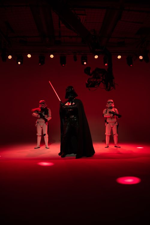 Free Three characters in sci-fi attire stand under dramatic red lighting indoors. Stock Photo