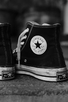 Close-up of well-worn Converse high-top sneakers on concrete surface, in black and white.