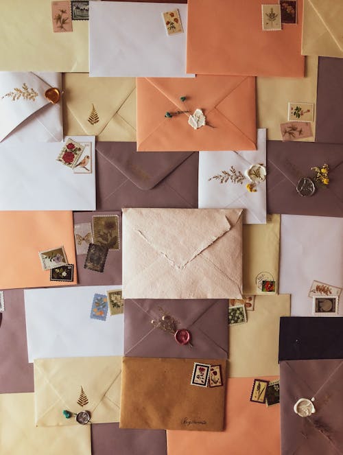 Top view composition of different colorful envelopes with stamps and sealing wax decorated with dry plants