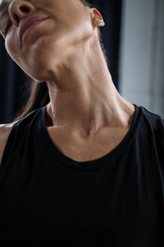 Close-up of a woman stretching her neck in a black tank top, focusing on health and flexibility.
