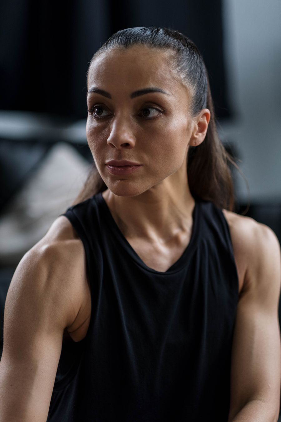 Coach Noor Haddad in a black training top, looking off-camera in a dim gym. Photo by Ron Lach on Pexels