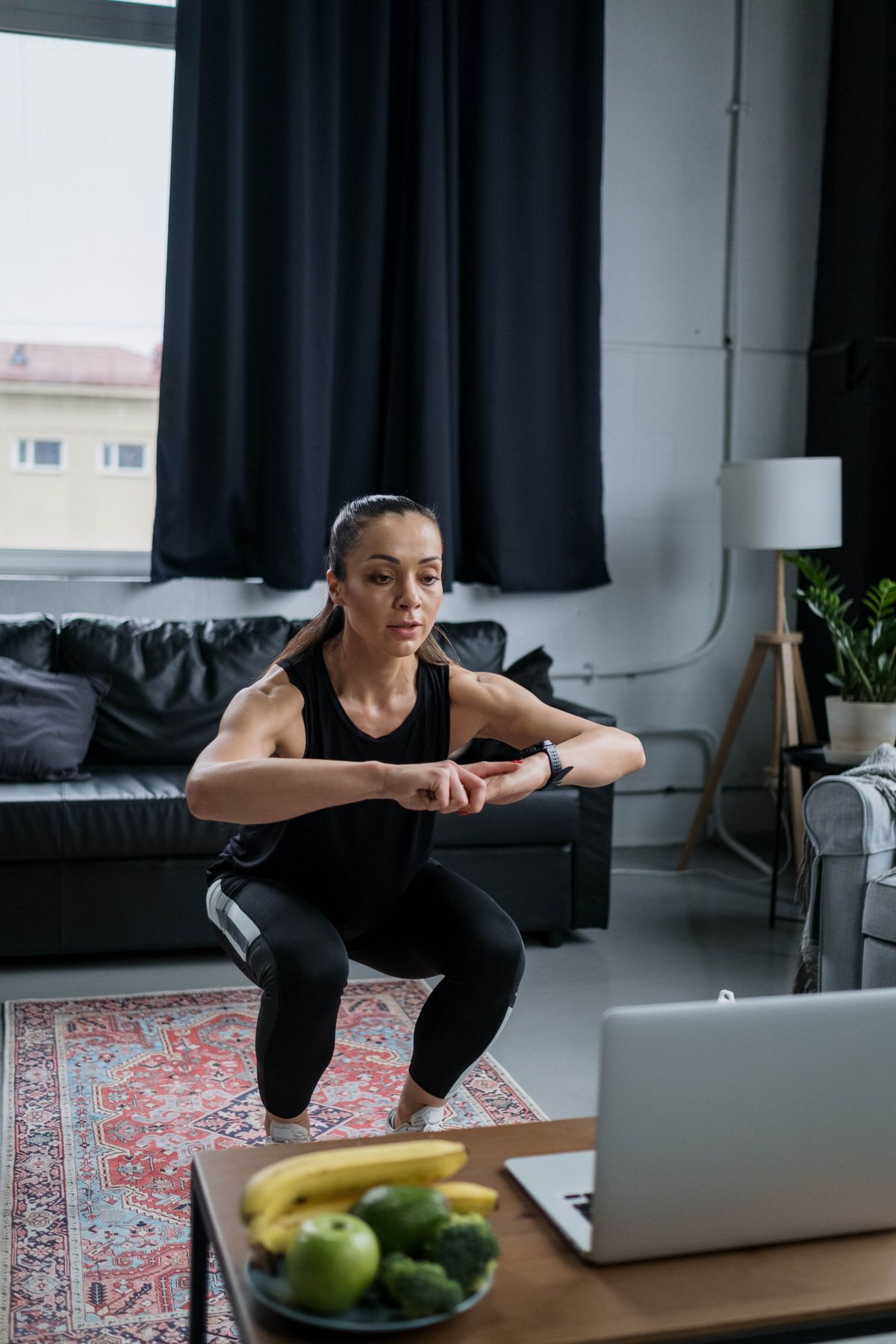 Woman performing a bodyweight squat in her living room with no equipment, building lower-body strength at home
