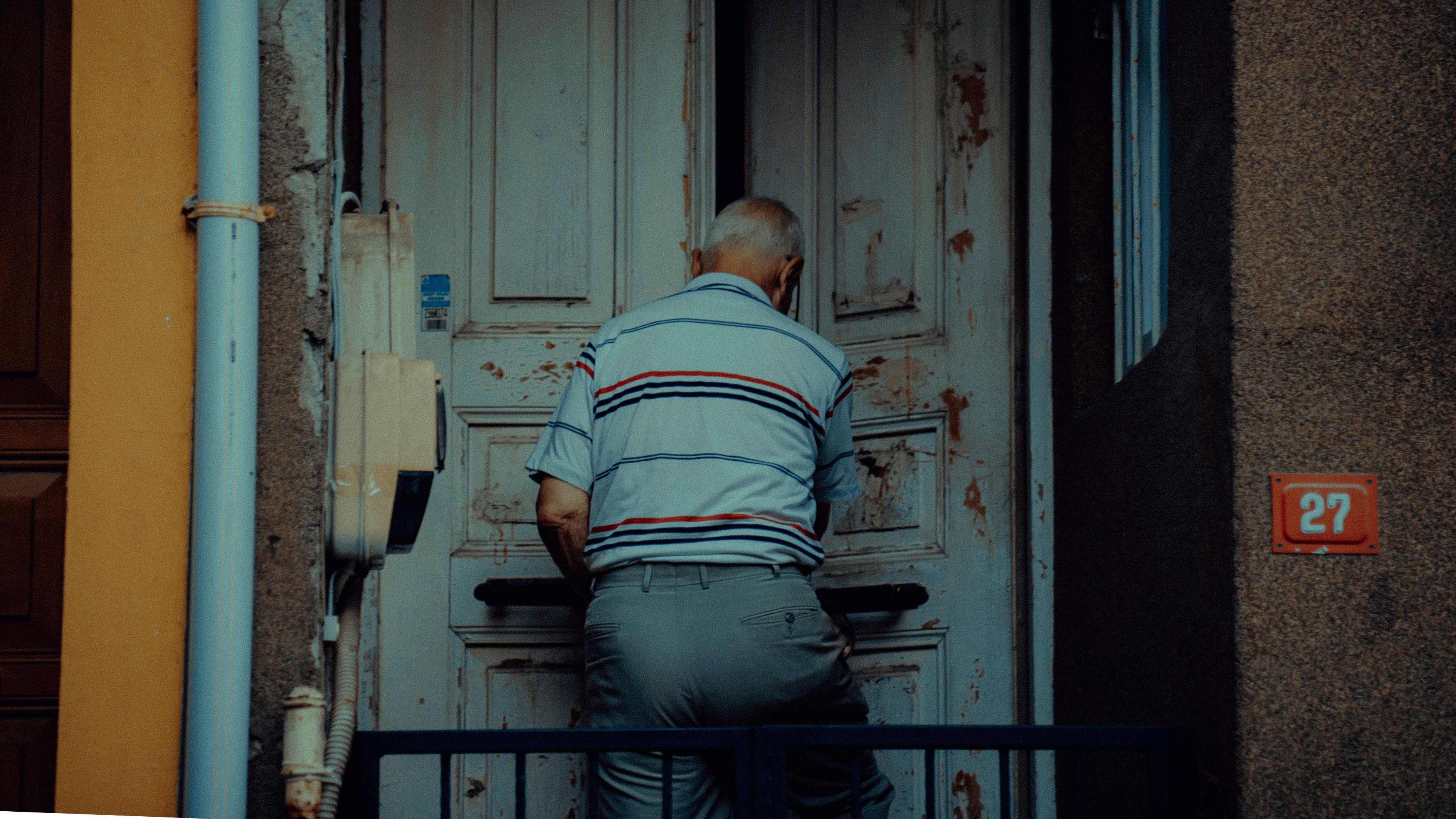Back view of unrecognizable elderly male in casual clothes entering building with shabby door in daytime