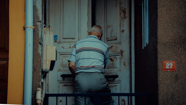 Senior Man Entering Building With Shabby Door