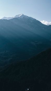 From above picturesque view of high mountains covered with snow and green coniferous trees under blue sky in daylight