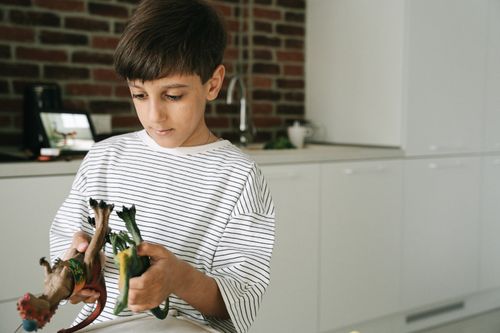 Free Young boy in striped shirt playing with dinosaur toys in a modern kitchen. Stock Photo