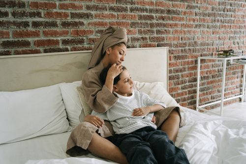 Free A tender moment between a mother and son in a stylish bedroom with brick wall decor. Stock Photo