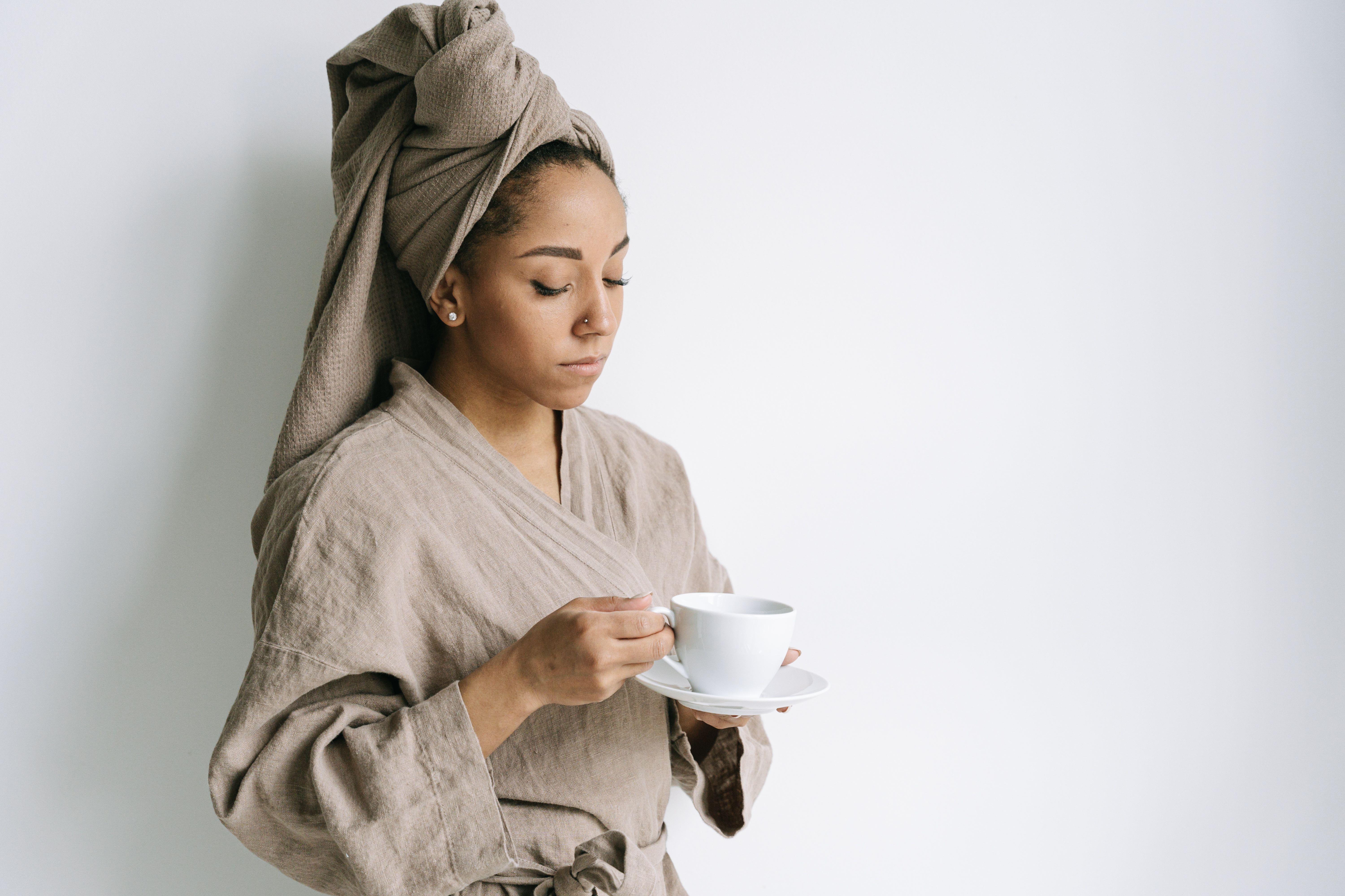 Serene woman in a bathrobe with a towel wrapped around her head, sipping coffee.