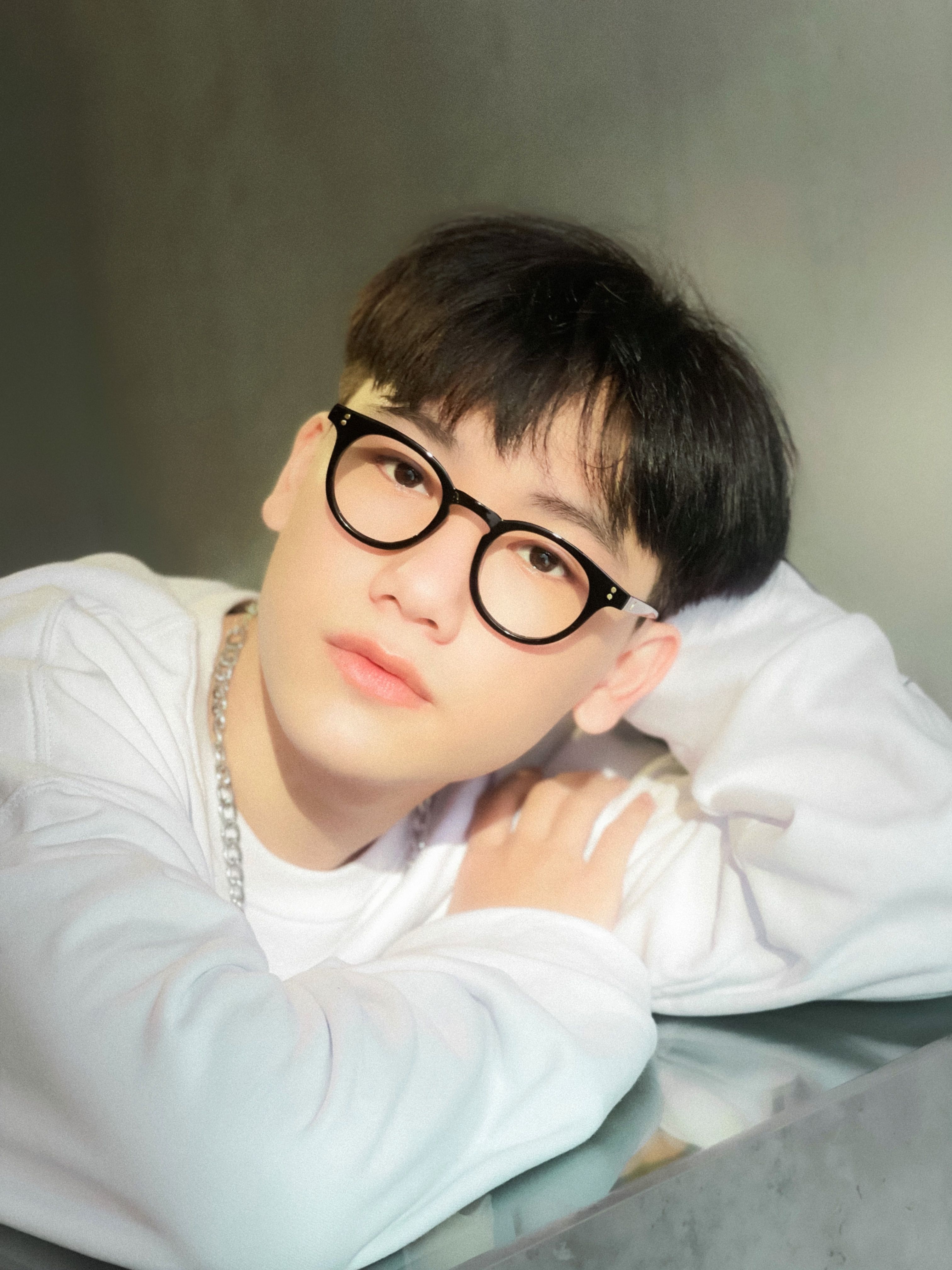 Teenager in a casual white shirt and eyeglasses posing indoors, highlighting modern style.