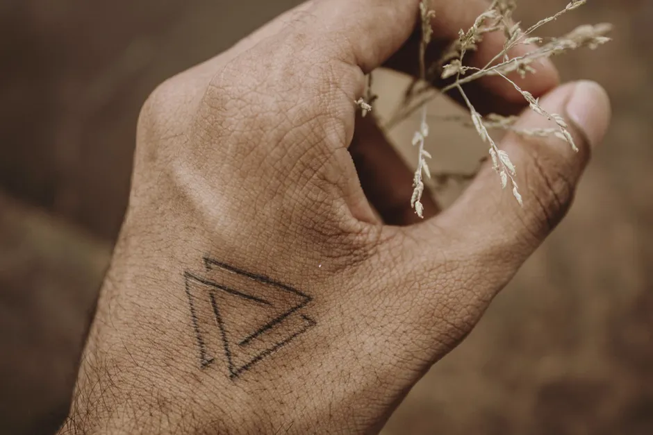 Close-up of a fine line geometric temporary tattoo on the hand, held near dried botanicals