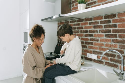 Free A mother and son enjoy quality time cooking together in a modern kitchen with brick accents. Stock Photo