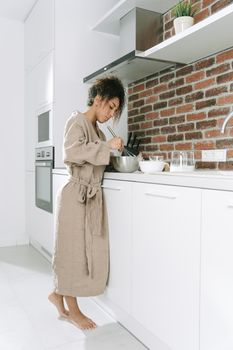 Black woman in a robe cooking breakfast in a modern kitchen setting.