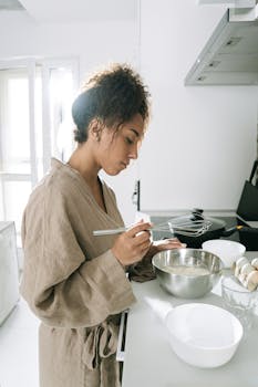 A woman preparing food in a bright kitchen, whisking ingredients in a bowl.