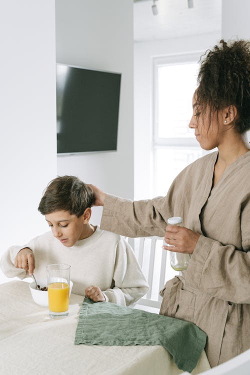 

A Boy Eating Breakfast beside His Mother