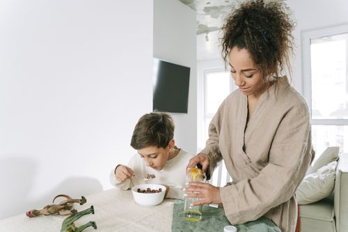 Free Mother in robe serves breakfast to her son as he eats cereal at home. Stock Photo