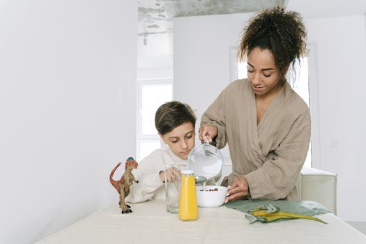 A warm morning scene of a mother helping her son with breakfast, pouring milk into a cereal bowl.