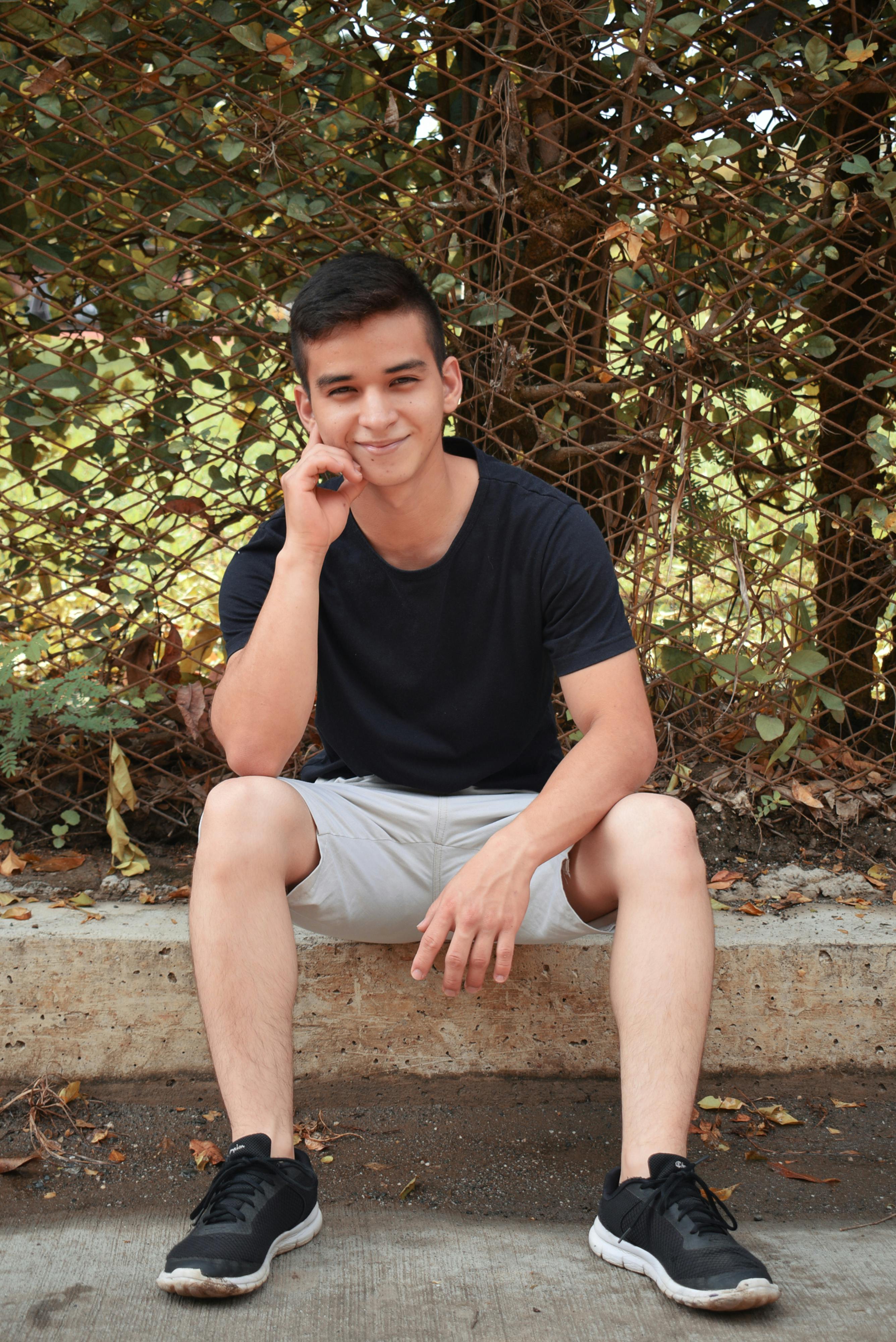 Young man in casual attire sitting outdoors, smiling at the camera.